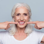 white-haired woman points at her teeth after a full smile restoration in Arlington, VA