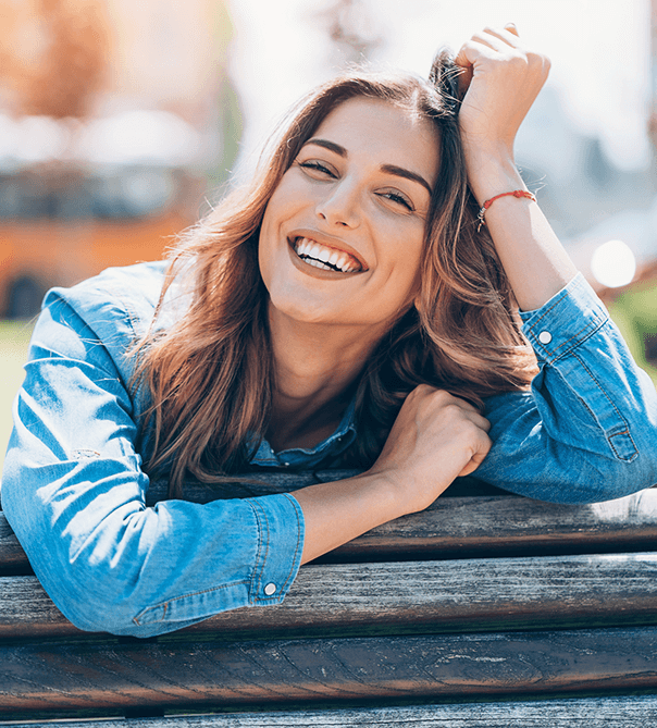 woman in denim jacket smiling and leaning on wood fence