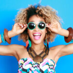Curly-haired woman smiles while wearing sunglasses after getting a makeover at the dentist with cosmetic dentistry