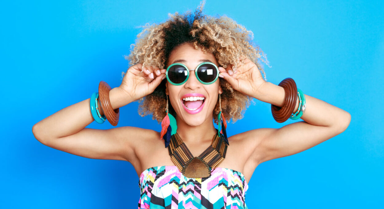 Curly-haired woman smiles while wearing sunglasses after getting a makeover at the dentist with cosmetic dentistry