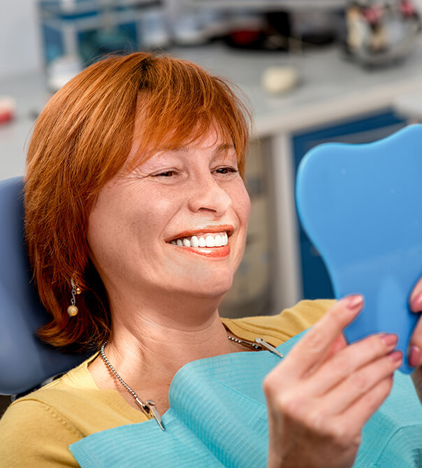 woman with red hair sitting in a dental chair and smiling at mirror