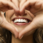 Closeup of a woman holding her hands in the shape of a heart in front of her smile