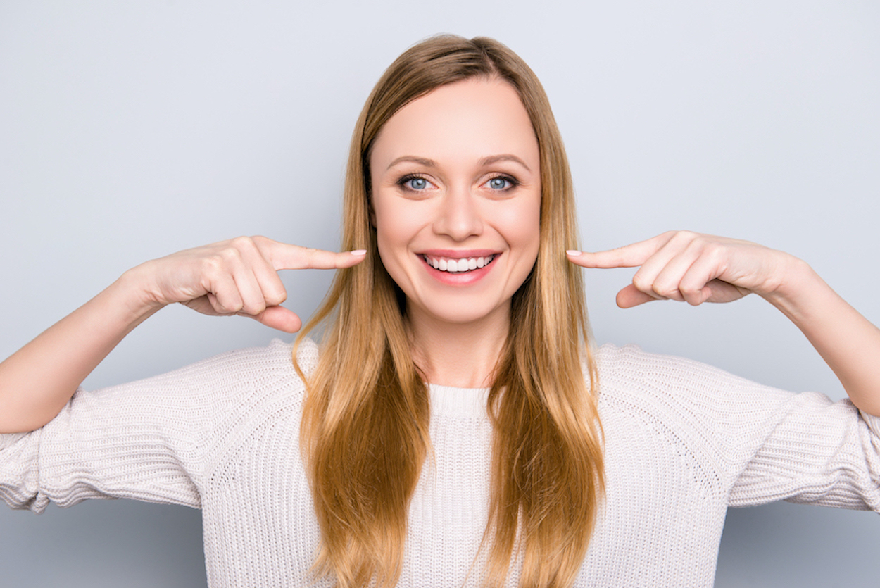 Blonde woman smiles and points to her teeth after straightening her teeth